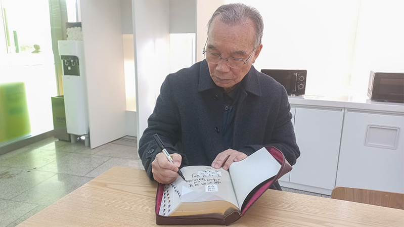 Pastor Kim Jin-Hong writing his signature on the bible for sending to President